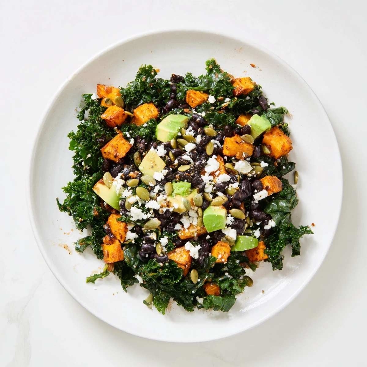 A large bowl of massaged kale salad with sweet potato, black beans, and pumpkin seeds, ready to eat.