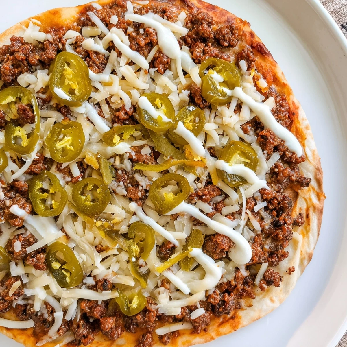 A sizzling Ground Beef Taco Pizza with a golden crust and a creamy sour cream drizzle.