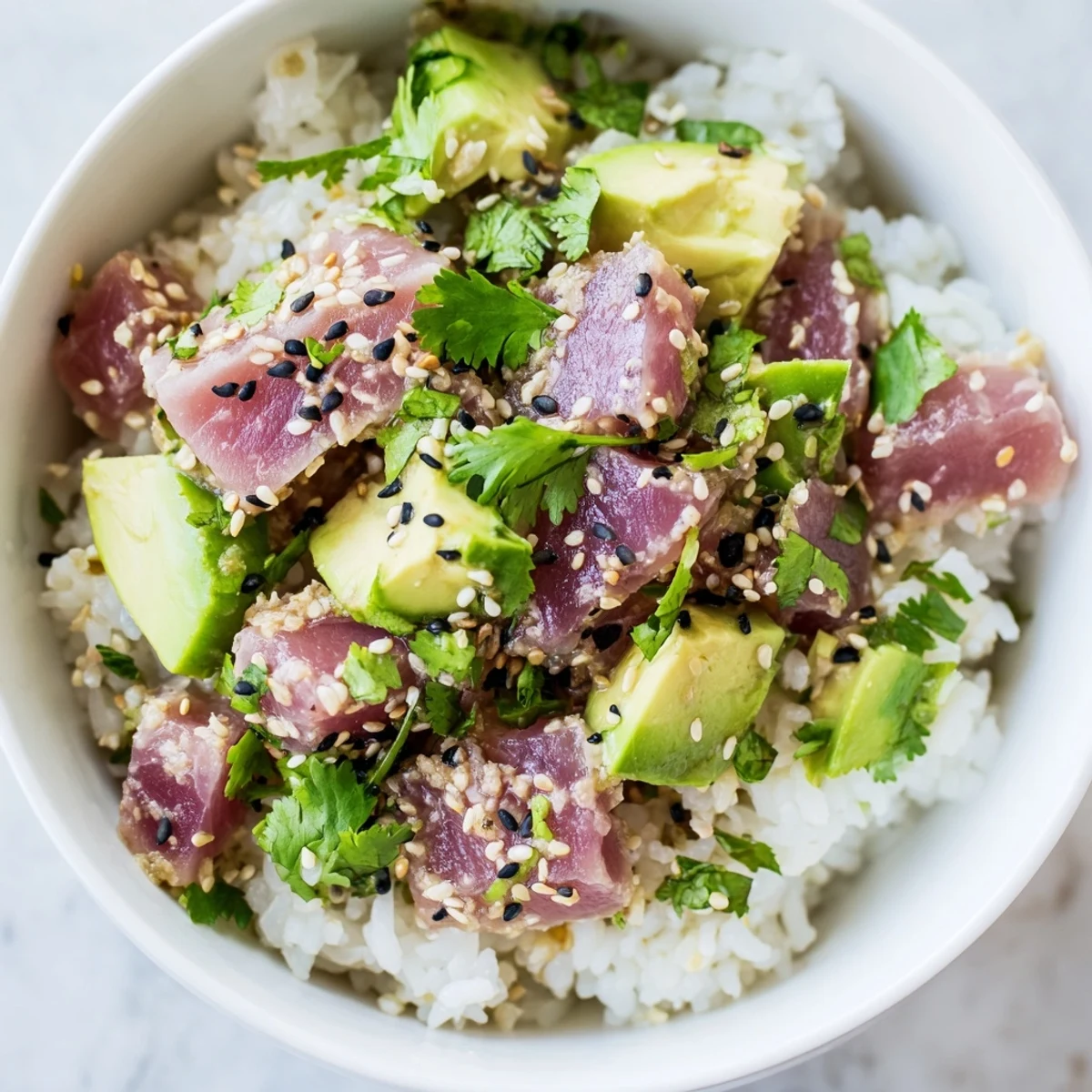 A vibrant Tuna Avocado Rice Bowl features creamy avocado chunks and tender tuna piled high on warm jasmine rice, garnished with crisp cucumber and toasted sesame seeds.