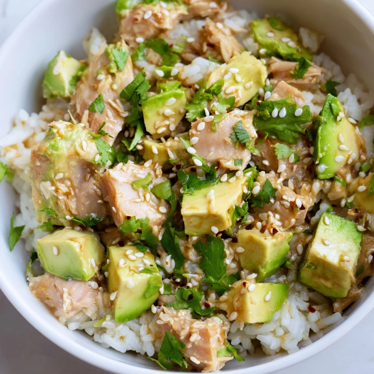 Hearty Tuna Avocado Rice Bowl with flaked tuna, diced avocado, and crisp cucumbers atop fluffy jasmine rice, drizzled with a savory-sweet sesame ginger dressing.
