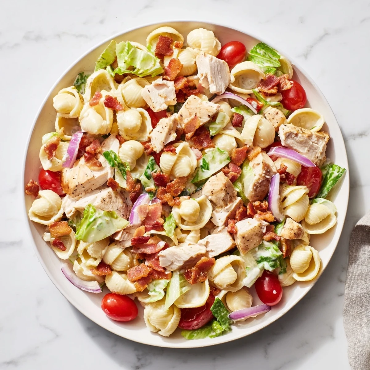 A fork rests beside tender pasta shells and chopped romaine, tossed in a light, tangy mayo dressing.