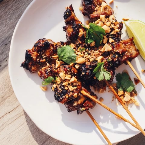 Grilled Spicy Peanut Satay Chicken Skewers, charred and glistening, served with fresh cilantro.