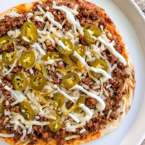 A sizzling Ground Beef Taco Pizza with a golden crust and a creamy sour cream drizzle.