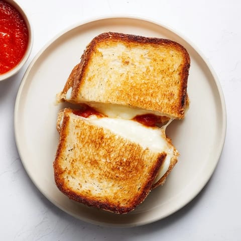 Golden-brown sourdough slices encase melted mozzarella cheese and crispy mozzarella sticks, creating a decadent grilled cheese sandwich perfect for dipping in warm marinara.  